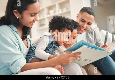 Quel son un singe fait. une jeune famille lisant un livre ensemble sur le canapé à la maison. Banque D'Images