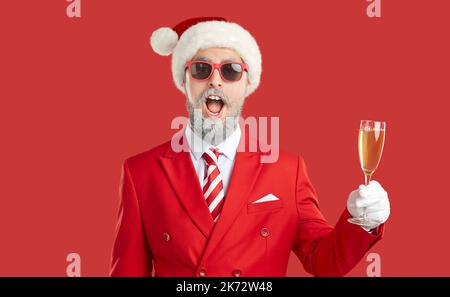 Portrait de drôle surpris barbu homme en costume de Noël tenant un verre de champagne Banque D'Images