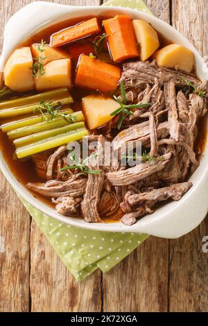 cuire lentement le bœuf tiré avec les pommes de terre, les oignons, les carottes, le céleri dans une sauce épicée dans une poêle à frire sur la table. vue verticale du dessus Banque D'Images