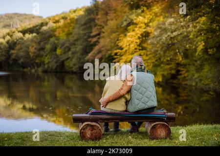 Couple senior amoureux assis sur le banc, en regardant le lac, pendant la journée d'automne. Vue arrière. Banque D'Images