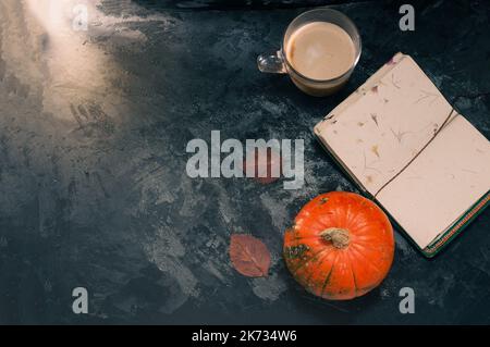 Une courge à la citrouille et un café latte à base de lait d'avoine ou de soja à base de plantes avec bloc-notes vierge à la table sur le b noir foncé Banque D'Images