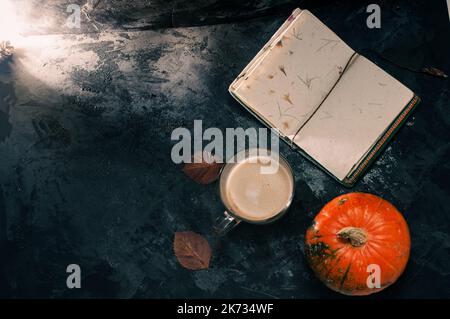 Une courge à la citrouille et un café latte à base de lait d'avoine ou de soja à base de plantes avec bloc-notes vierge à la table sur le b noir foncé Banque D'Images