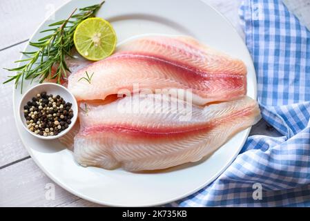 Poisson dolly à la viande tilapia poisson-chat rayé, filet de poisson pangasius frais cru avec herbes et épices citron vert et romarin, filet de poisson sur plaque blanche avec Banque D'Images