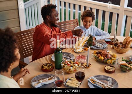 Vue latérale portrait d'un homme noir souriant qui verse des boissons dans des verres tout en appréciant un dîner en famille à l'extérieur Banque D'Images