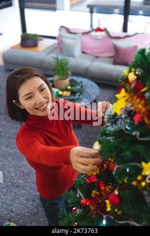 Bonne femme asiatique décorant arbre de noël dans la salle de séjour Banque D'Images