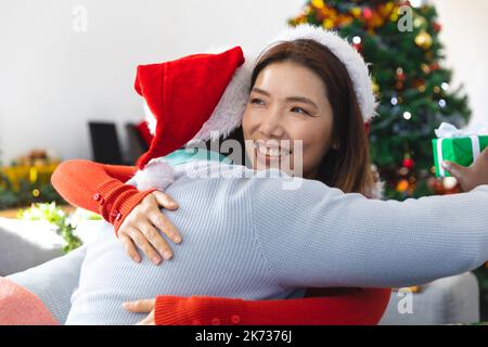 Joyeux couple divers portant des chapeaux de père noël, assis sur un canapé, déballer des cadeaux Banque D'Images