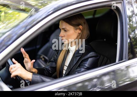 Jeune femme part en appuyant sur le bouton du klaxon au volant d'une voiture par la route. Banque D'Images