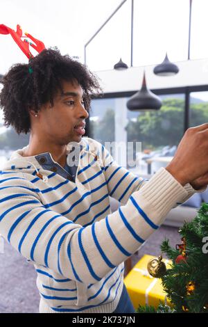 Joyeux homme américain africain décorant l'arbre de noël dans la salle de séjour Banque D'Images