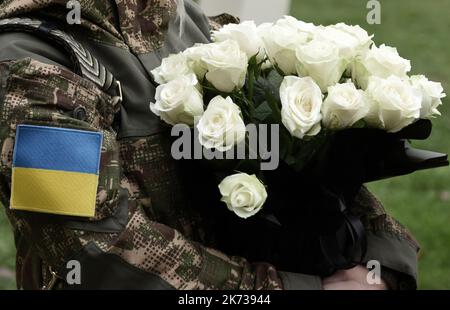 Drapeau ukrainien sur l'uniforme militaire. Le soldat tient des fleurs. Funérailles de militaires ukrainiens. Banque D'Images