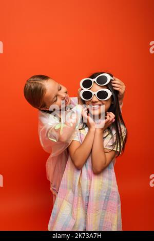 fille souriante mettant deux lunettes de soleil sur ami souriant isolé sur orange Banque D'Images