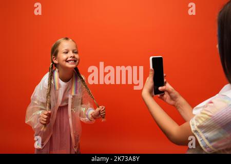 drôle de fille tenant ses picots près de l'ami prenant la photo sur smartphone isolé sur orange Banque D'Images