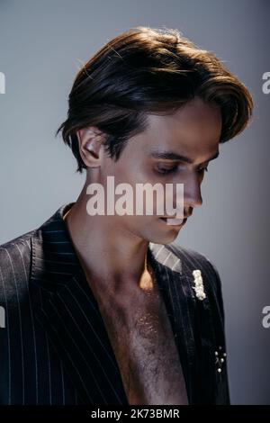 portrait d'un homme brunette avec poitrine velue et blazer rayé élégant sur gris foncé Banque D'Images