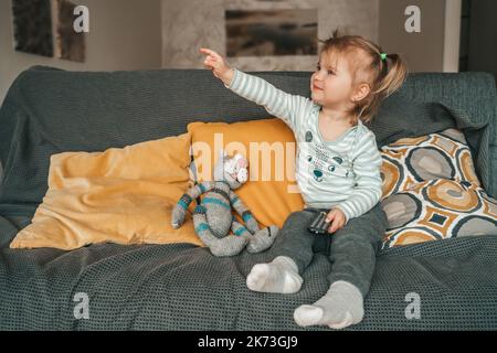 Petite fille avec un accessoire TV assis sur le canapé Banque D'Images