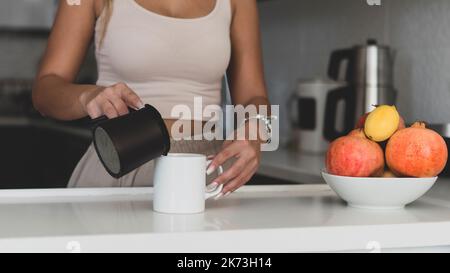 maquette de tasse blanche. Une jolie femme dans une cuisine moderne verse le café dans une tasse blanche vide Banque D'Images