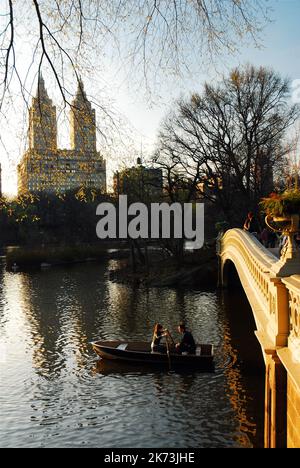 Un couple conduit leur barque sur le lac dans Central Park sous le pont Bow et en vue des appartements San Remo à New York Banque D'Images