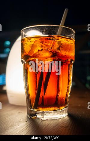 Rhum blanc et coke avec de la glace dans un verre avec un dos de paille éclairé par une lampe de table Banque D'Images