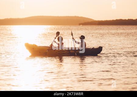 Deux rameurs sur l'aviron de kayak gonflable par le coucher du soleil raies mer Adriatique port en Croatie près de la ville de Sibenik. Vacances, sports et loisirs Banque D'Images