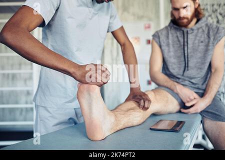 Gros plan d'un thérapeute africain faisant un massage au patient sur sa jambe pendant qu'il est assis sur le canapé Banque D'Images