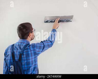 Jeune homme adulte main à l'aide d'une spatule et plâtrage mur blanc avec du mastic de finition frais. Gros plan. Travaux de réparation à domicile. Banque D'Images
