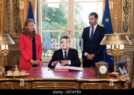 Le président français Emmanuel Macron (C), flanqué de la ministre de la Justice Nicole Belloubet et de la ministre déléguée aux relations avec le Parlement et porte-parole du gouvernement Christophe Castaner (R), signe des documents pour promulguer les projets de loi de foi dans la vie politique française sur 15 septembre 2017 dans son bureau à l'Elysée à Paris. Banque D'Images