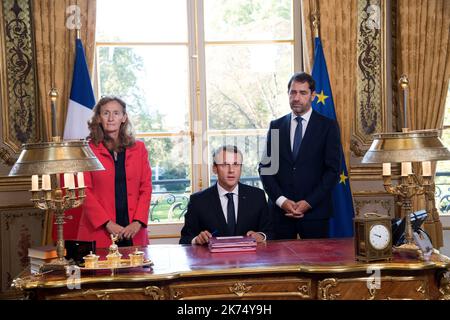 Le président français Emmanuel Macron (C), flanqué de la ministre de la Justice Nicole Belloubet et de la ministre déléguée aux relations avec le Parlement et porte-parole du gouvernement Christophe Castaner (R), signe des documents pour promulguer les projets de loi de foi dans la vie politique française sur 15 septembre 2017 dans son bureau à l'Elysée à Paris. Banque D'Images