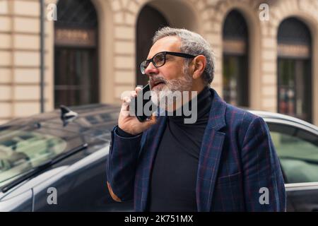 Homme d'affaires mûr à cheveux gris élégant et sûr de lui-même parlant au téléphone alors qu'il se présente au travail. Photo de haute qualité Banque D'Images