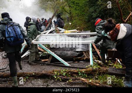 Les manifestants se protègent des gaz lacrymogènes sur la route D281 lorsqu'ils s'opposent à la police anti-émeute dans la ZAD (zone de défense a) à notre-Dame-des-Landes, dans l'ouest de la France, sur 9 avril 2018. Plus de 2 000 policiers français ont pris part à 10 avril à l'expulsion des derniers récalcitrants d'un camp anticapitaliste sur le site d'un projet d'aéroport abandonné près de la ville occidentale de Nantes. Les officiers ont essaié le site de notre-Dame-des-Landes avant l'aube pour expulser environ 100 des manifestants qui l'avaient occupé pour empêcher la construction d'un aéroport controversé, puis ont refusé de faire le vol Banque D'Images