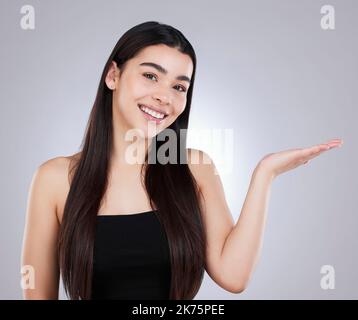 Heres mon conseil à vous pour la belle peau et les cheveux. Studio portrait d'une jeune femme attrayante pointant vers le copyspace sur un fond gris. Banque D'Images