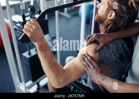 Jeune patient entraînant sa blessure bras sur l'équipement d'exercice dans la salle de gym tout en thérapeute le massant Banque D'Images