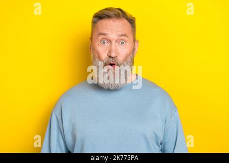 Photo d'excitée choqué à la retraite gars porter bleu chandail grands yeux isolé couleur jaune arrière-plan Banque D'Images