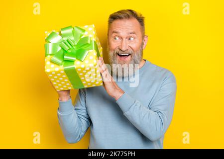 Photo de l'excitée funky retraité gars porter bleu chandail bras bouche deviner ce qui à l'intérieur de la boîte actuelle isolé couleur jaune fond Banque D'Images