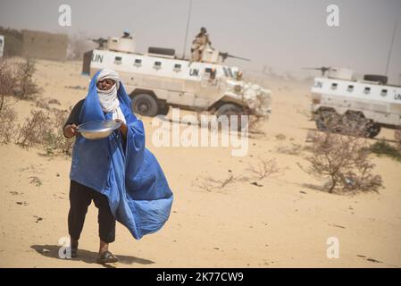 Un Tuareg porte un plat alimentaire et derrière lui les casques bleus de la MINUSMA s'assurent de la vieille école où une délégation du HCR et de la MINUSMA est en visite, accompagnée du gouverneur de la région de Tombouctou Koina AG Ahmadou, à Koygouma (cercle de Goundam) dans la région de Tombouctou, sur 6 mai 2019. Cette visite fait suite au rapatriement de 2086 réfugiés maliens du camp de Mbera en Mauritanie en avril dernier, qui ont dû fuir le conflit en 2013. Banque D'Images