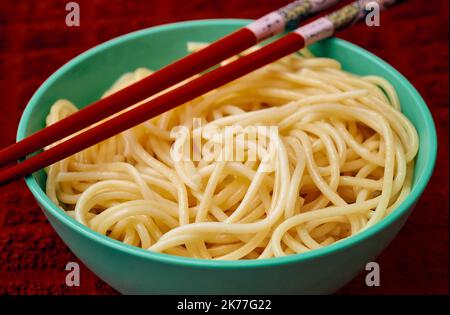 Les pâtes de semoule bio sont servies dans un petit bol sarcelle avec une baguette rouge sur un toll de cuisine rouge Banque D'Images