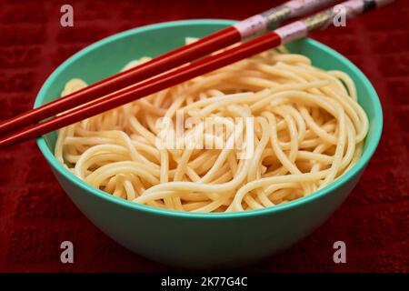 Les pâtes de semoule bio sont servies dans un petit bol sarcelle avec une baguette rouge sur un toll de cuisine rouge Banque D'Images