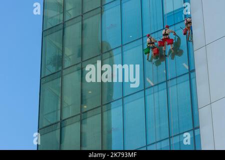 Nettoyeurs de fenêtres anonymes nettoyant les fenêtres dans les balançoires ou les berceaux à l'extérieur d'un gratte-ciel de ville Banque D'Images