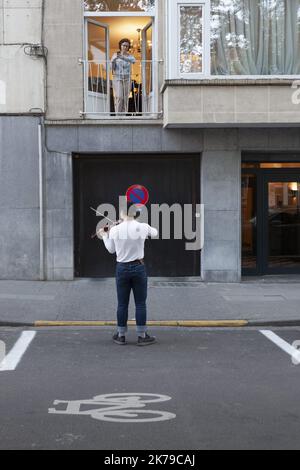 Belgique / Bruxelles / Bruxelles - Un jeune homme joue le violon dans la rue pour ses voisins dans des bâtiments et en soutien au personnel infirmier. Banque D'Images