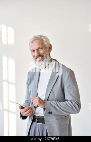 Homme d'affaires souriant et âgé utilisant une tablette isolée sur un mur blanc, à la verticale. Banque D'Images