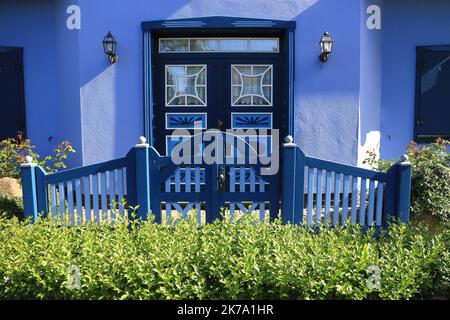 Façade bleue d'une maison moderne avec porte d'entrée derrière une clôture en bois et une haie verte Banque D'Images