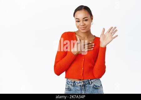 Belle femme noire de 20 ans, levant la main, agitant, se présenter et saluant, debout sur fond blanc Banque D'Images