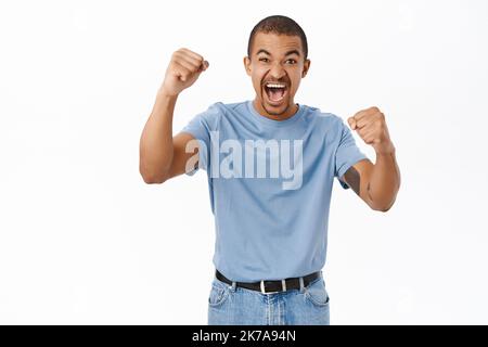 Un homme arabe enthousiaste criant, applaudisant, regardant un match de sport et se tenant pour l'équipe, debout sur fond blanc Banque D'Images