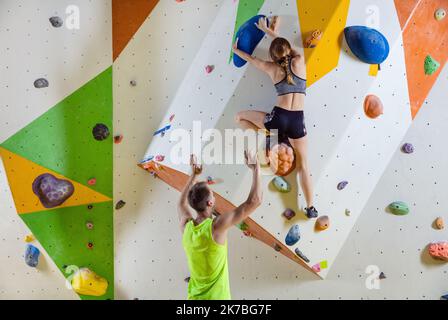 Grimpeurs en escalade. Jeune femme escalade bouldering problème (route), de sécuriser les instructeurs masculins. Banque D'Images