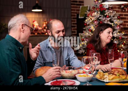 Joyeux Noël en famille, les gens parlent à table de fête, manger la nourriture traditionnelle des fêtes d'hiver, bavarder. Fête de Noël avec les parents à la maison Banque D'Images