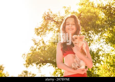 Adolescente gaie dans un maillot de bain rouge en vacances. Une fille et un chihuahua blanc. Banque D'Images