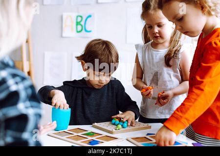 Les jolis petits enfants plient les détails du constructeur sur le bureau dans la salle de jeux de près. Jeu intéressant pour les jardins d'enfants développant la logique et l'intelligence Banque D'Images