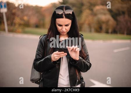 Une jeune femme sérieuse qui utilise un smartphone lorsqu'elle se trouve sur la route fait le choix de la direction à suivre Banque D'Images