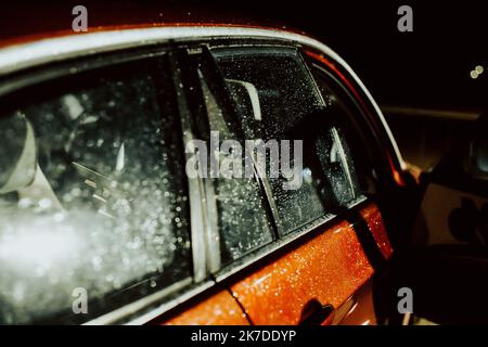 Voiture rouge sous la pluie tard dans la nuit, de l'eau tombe sur le verre. Pluie Banque D'Images