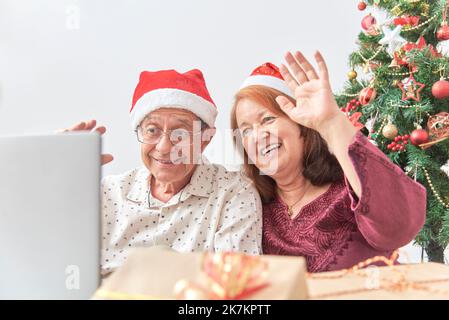 Un couple hispanique d'âge mûr accueille ses proches par appel vidéo pendant les fêtes à l'aide d'un ordinateur portable. Concepts: La joie de partager pendant les vacances, le Banque D'Images