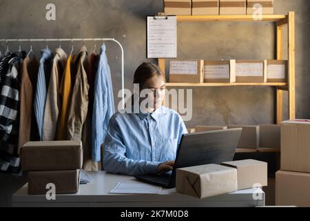 Boutique en ligne vendant des vêtements sur le site Web travaillant sur ordinateur portable ecommerce affaires de la maison. Femme vendre de nouveaux vêtements, mode achat expédition. Banque D'Images