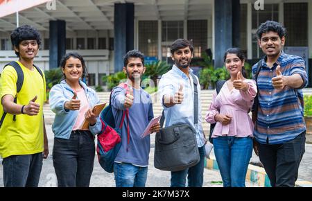 Des étudiants confiants avec un sac à dos et des livres montrant le pouce vers le haut en regardant la caméra sur le campus universitaire - concept d'approbation, éducation et développement. Banque D'Images