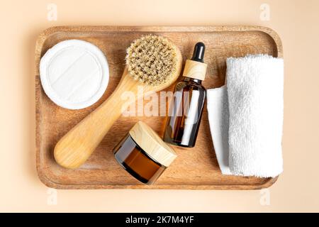 vue de dessus du plateau en bois avec produits d'entretien du visage. Huile de beauté et crème quotidienne en verre foncé. Brosse pour le visage et serviette en coton. Soins spa. Organe Banque D'Images
